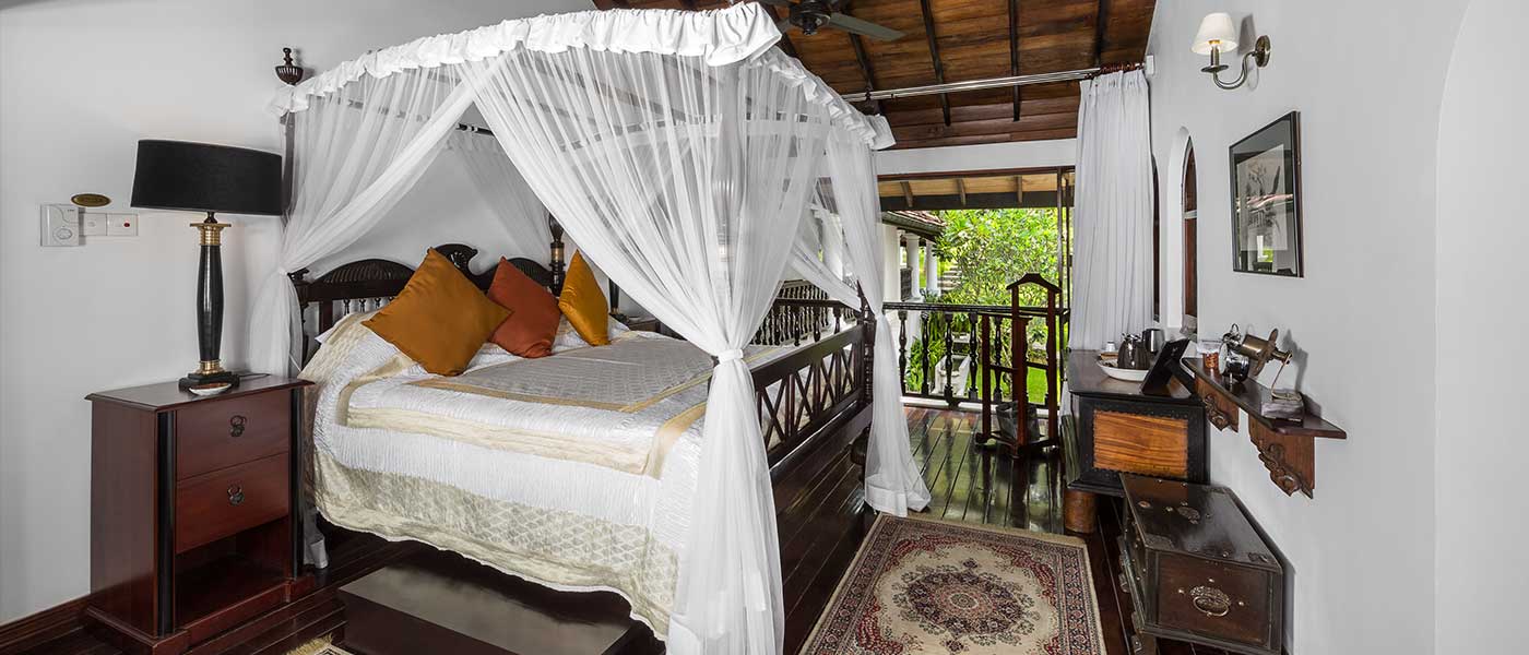 A suite with a netted four-poster bed, dark timber furniture and a rug on a polished floor